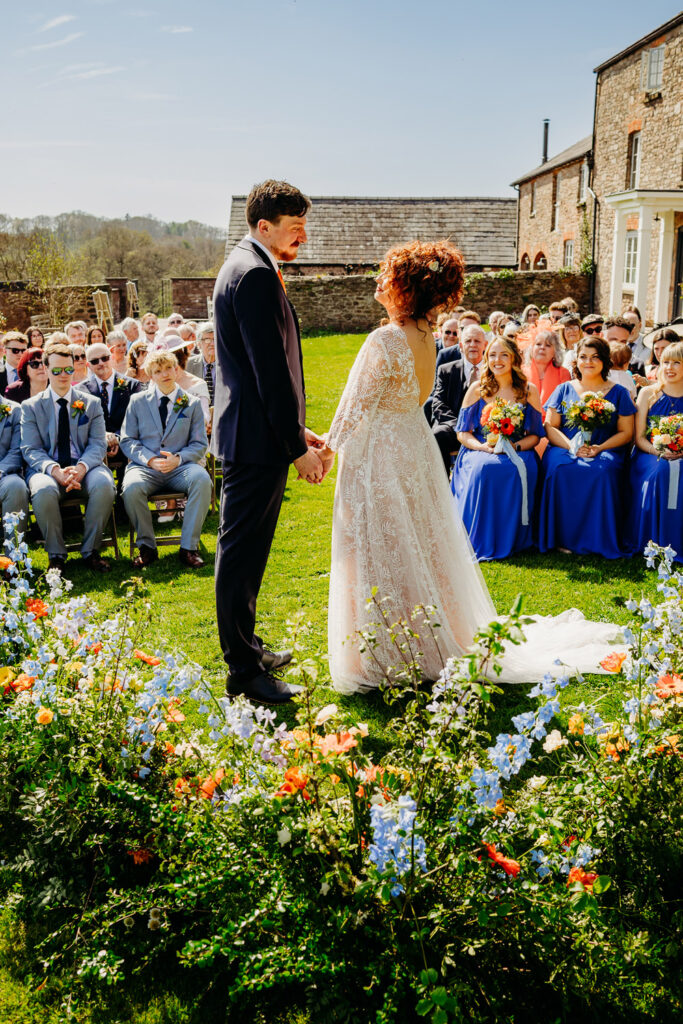 A bride and groom in between their guests and a floral meadow in an outdoor ceremony