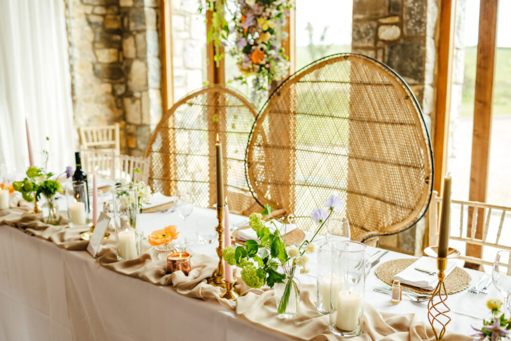 Beautifully styled wedding top table with wicker chairs, flowers and candles in pastel shades