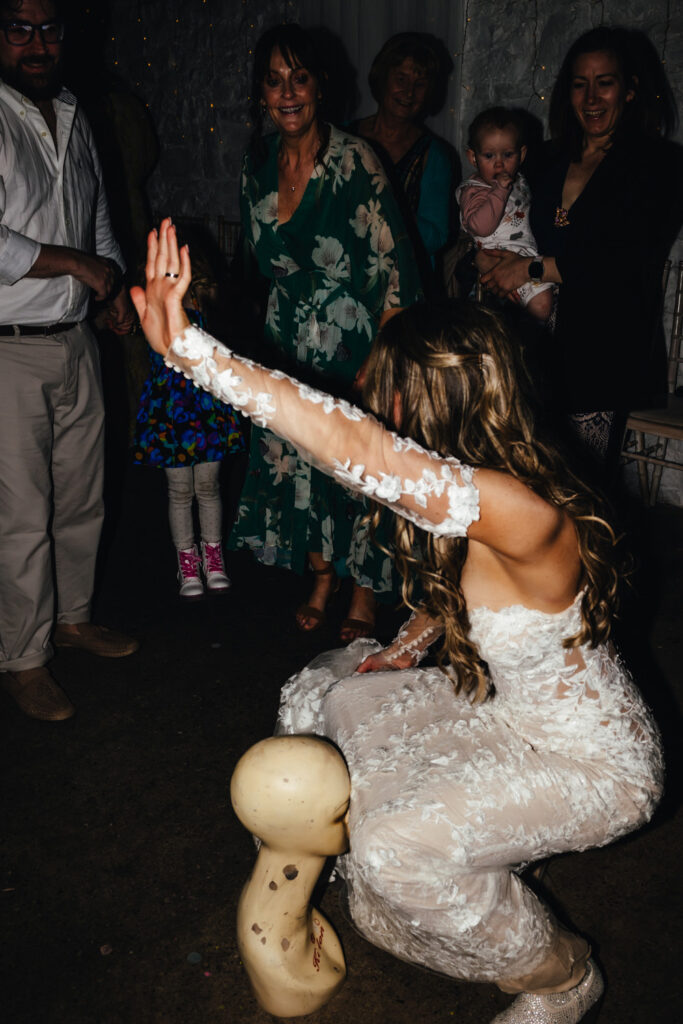 Bride on the dancefloor, one arm in the air, dancing around a mannequin head