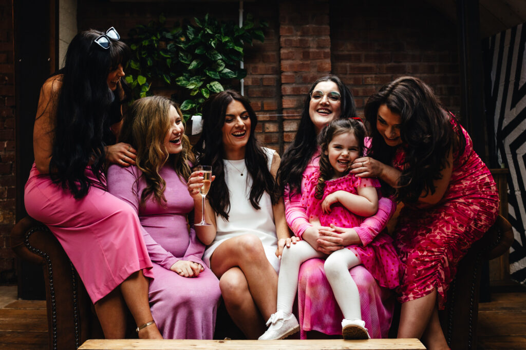 A bride and her bridesmaids squished together on a sofa, laughing