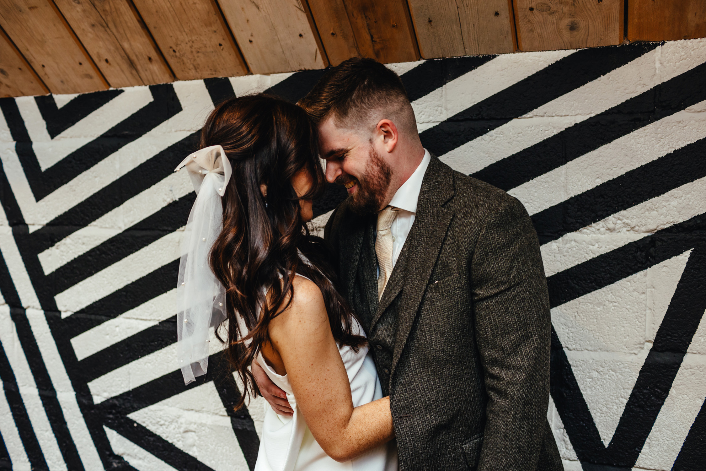 Bride and groom touching foreheads in an intimate pose in front of a geometric background