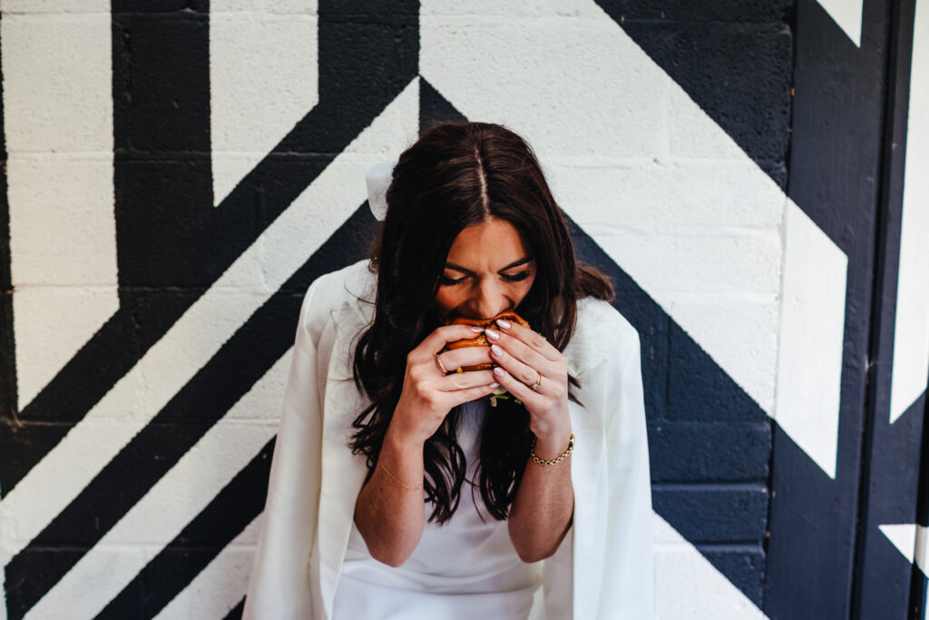 cool, modern looking Bride eating a burger in front of a monochrome, geometric patterned wall.