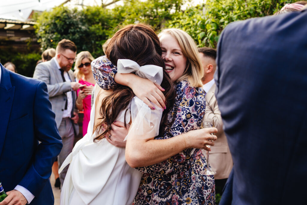 A bride wearing a white bow in her hair hugging one of her guests