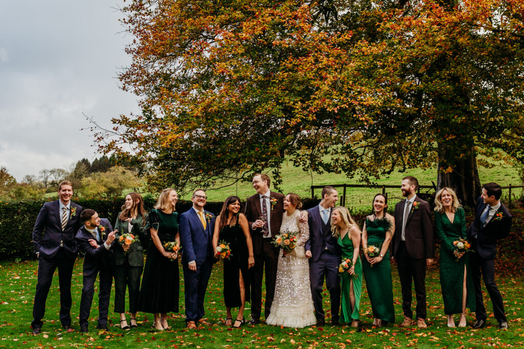 A wedding party are standing in a row, looking at each other and laughing