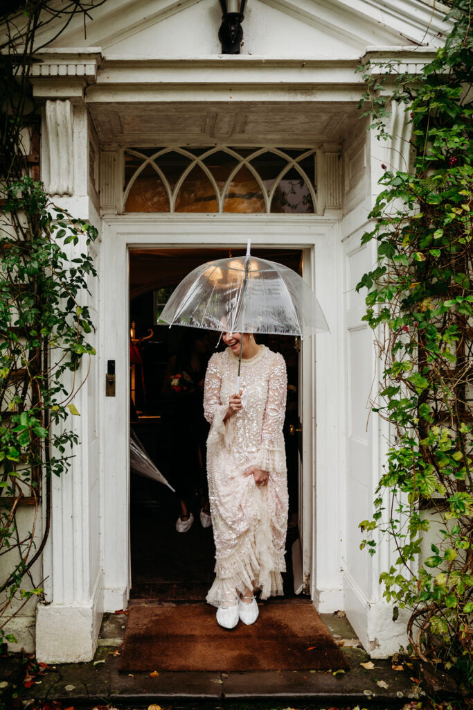 A bride in a doorway, holding an umbrealla and wearing shoe covers