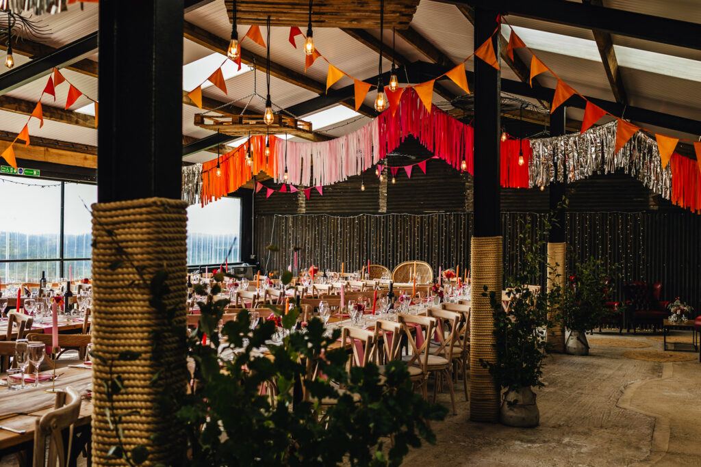 A barn wedding venue decorated with red, pink, orange and silver bunting