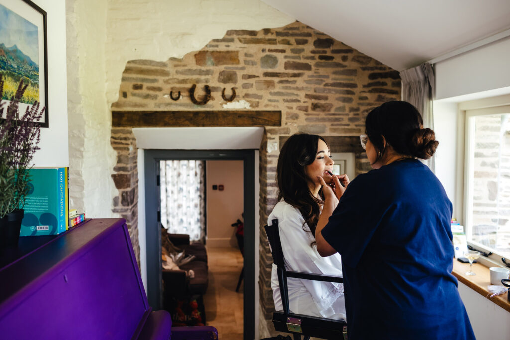 A bride having her make up done by a make up artist in front of a window