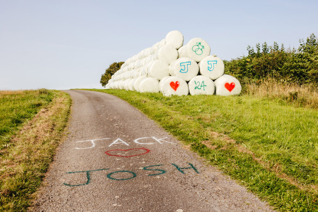 Hay bales spray painted with J+J with man and man symbols and hearts, next to Jack heart Josh spray painted on the lane