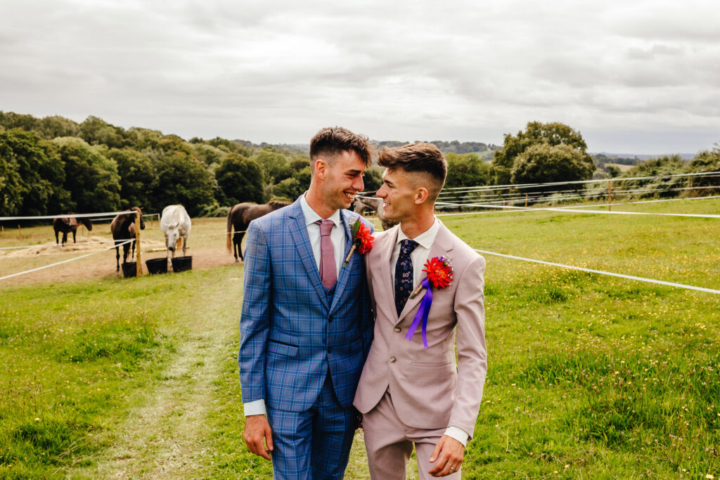 Two grooms, one in pink and one in blue, walking through their farm with horses in the background