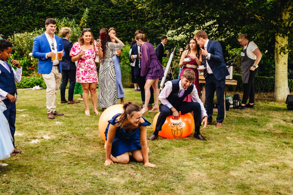 A space hopper race at a wedding, a man is on an orange space hopper, a woman has fallen off. 