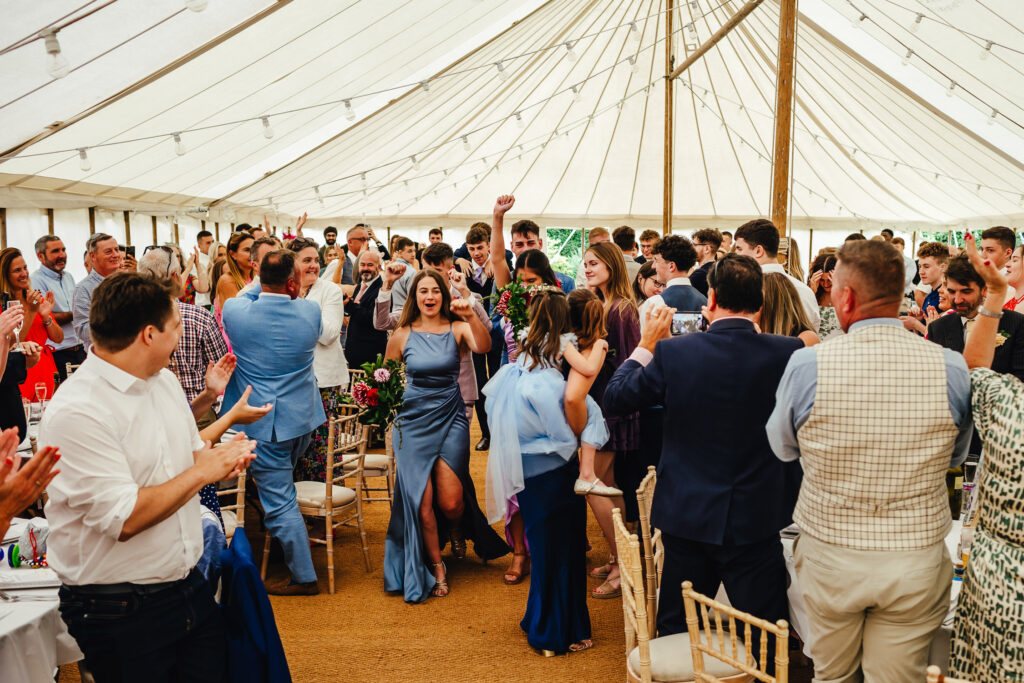 A wedding party dancing their entrance into a marquee full of wedding guests